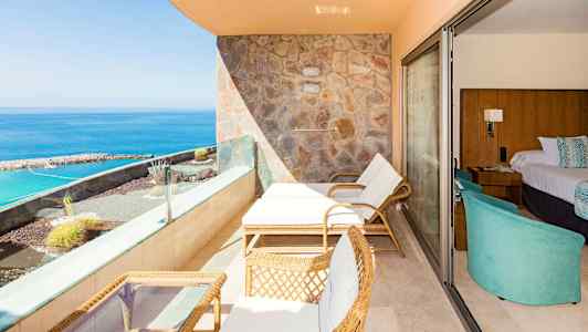 En terrass med solstolar, bord och havsutsikt, bredvid ett hotellrum. (AI-genererad text)