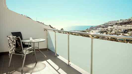 Balkong med bord och stol, utsikt mot hav och bebyggelse. (AI-genererad text)