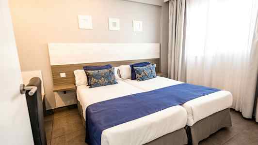 Hotellrum med två enkelsängar bredvid varandra, blå överkast och dekorativa kuddar. (AI-genererad text)