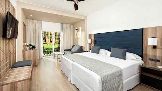 Ett modernt hotellrum med en stor säng, sittmöbler och ett glasparti med utsikt över en grönskande trädgård. (AI-genererad text)