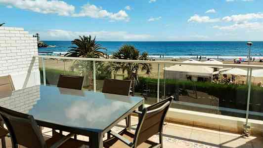 En möbelgrupp på en balkong med utsikt över stranden och havet. (AI-genererad text)