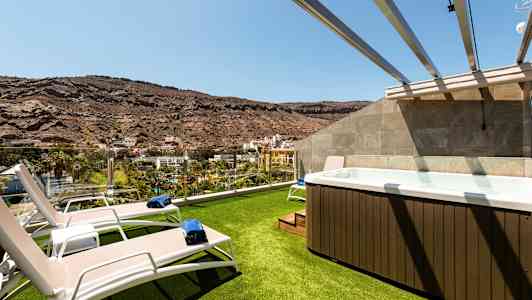 Bild av en terrass med gräsklädd yta, solstolar och en jacuzzi med utsikt över ett bergslandskap. (AI-genererad text)