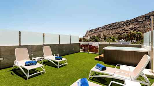 Terrass med solstolar, badhanddukar och jacuzzi, omgiven av glasräcke och utsikt över berg. (AI-genererad text)