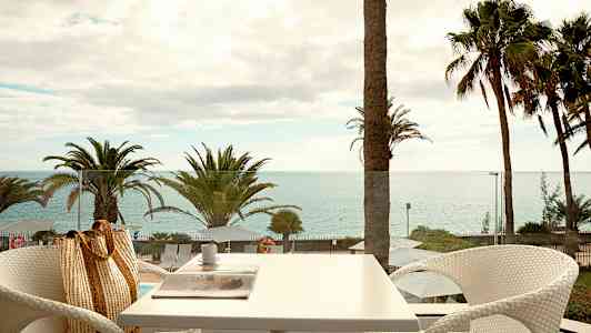 Utsikt från en terrass med havet i bakgrunden och palmträd. (AI-genererad text)