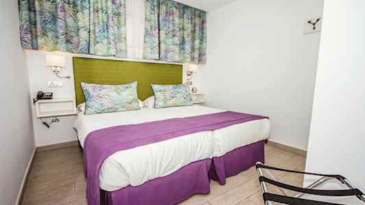 Sovrum med en dubbelsäng, grönt sänggavel, lila överkast och gardiner med mönster. (AI-genererad text)