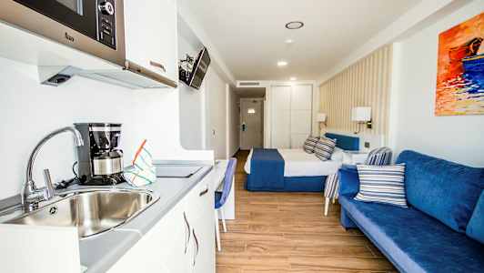 Ett hotellrum med en säng, blå soffa och köksdel med diskho. (AI-genererad text)