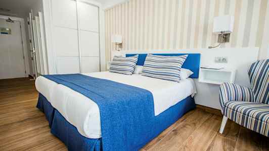 En smakfull hotellrum med en dubbelsäng täckt av blå och vit sängkläder samt randiga kuddar, vid sidan av ett randigt fåtölj. (AI-genererad text)