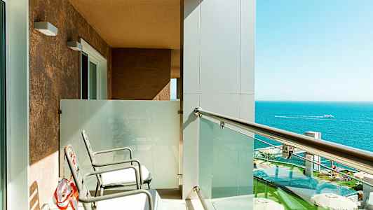 Balkong med två stolar, glasräcke och utsikt över havet. (AI-genererad text)