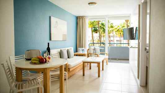 Ett vardagsrum med ett matbord och stolar, samt en soffa nära glasdörrar som leder till en balkong. (AI-genererad text)