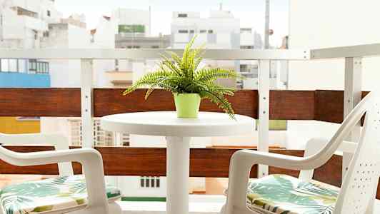 En balkong med ett bord och två stolar, en grön krukväxt på bordet. (AI-genererad text)