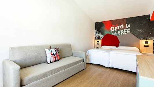 Ett modernt hotellrum med en grå soffa, en dubbelsäng och dekorativ vägg med text. (AI-genererad text)