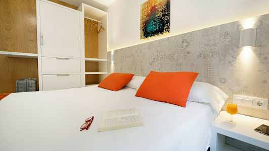 Sovrum med vit dubbelsäng, orange kuddar och öppet klädskåp. (AI-genererad text)