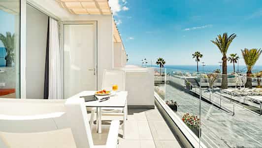 En solig terrass med utsikt över havet, utrustad med en vit sittgrupp. (AI-genererad text)