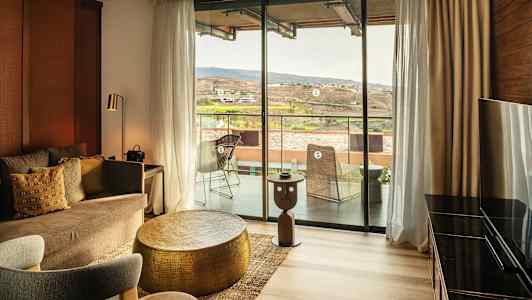 En inredd hotellsvit med en sittgrupp och utsikt mot en balkong och landskap. (AI-genererad text)