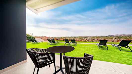 En uteplats med bord, stolar, gräsmatta och solstolar, med utsikt över landskapet. (AI-genererad text)