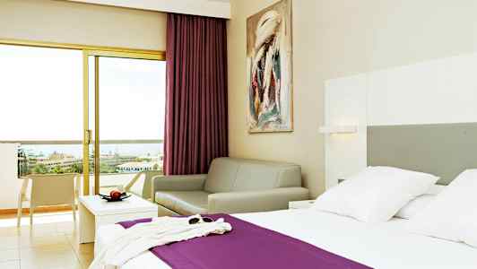 Hotellrum med en säng, en soffa och en balkong med utsikt. (AI-genererad text)