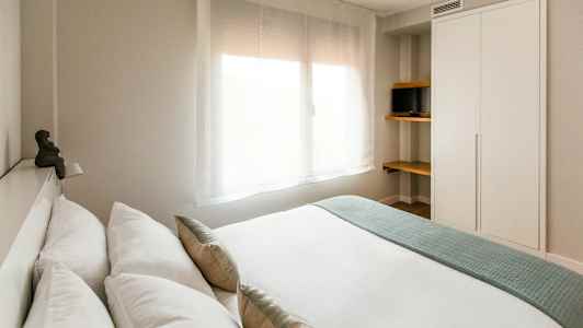 Modernt sovrum med en stor fönsterruta, en garderob och hyllor med en liten tv. (AI-genererad text)