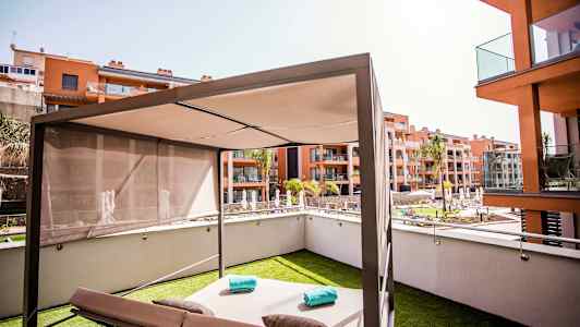 En modern solbädd med parasoll på en gräsmatta, omgiven av bostadshus och en pool. (AI-genererad text)