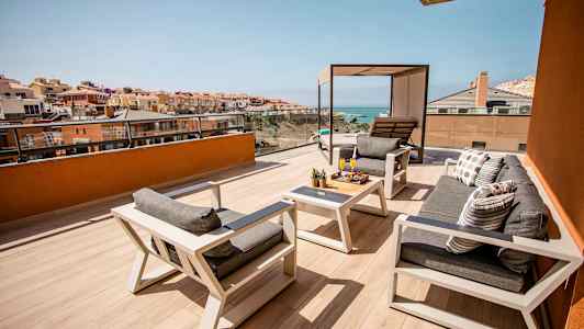 En rymlig terrass med sittmöbler och bord, utsikt över havet och omgivande byggnader. (AI-genererad text)