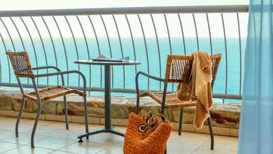 Utsikt över havet från en balkong med bord, två stolar och en strandväska. (AI-genererad text)