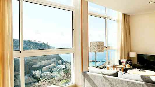 Vardagsrum med stora fönster som visar utsikt över havet och en klippa. (AI-genererad text)