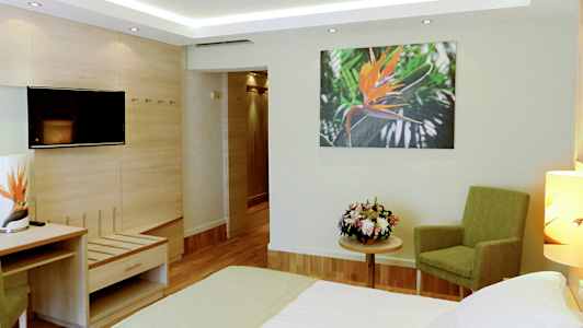 Ett hotellrum med en säng, grön stol, blombukett på ett bord och en väggbild av en orange blomma. (AI-genererad text)