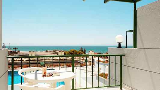 En balkong med utsikt över en pool och havet, bord och stolar synliga. (AI-genererad text)
