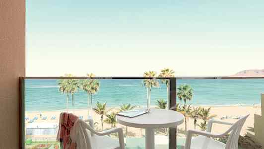 Balkong med utsikt över strand och hav, bord och stolar synliga. (AI-genererad text)