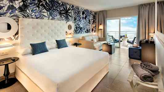 Hotellrum med en stor säng, sittgrupp och balkong med utsikt. (AI-genererad text)