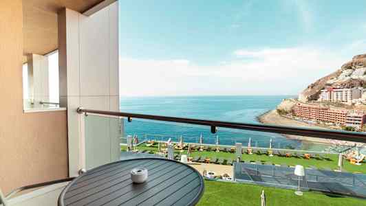 Utsikt från en balkong mot havet och en grönskande hotellträdgård. (AI-genererad text)