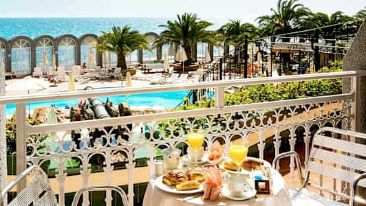 Utsikt från en balkong med frukostdukning mot poolområde och havet. (AI-genererad text)