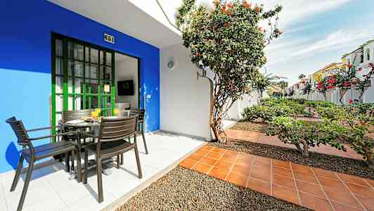 Terrass med bord och stolar, omgiven av växter och blommor. (AI-genererad text)