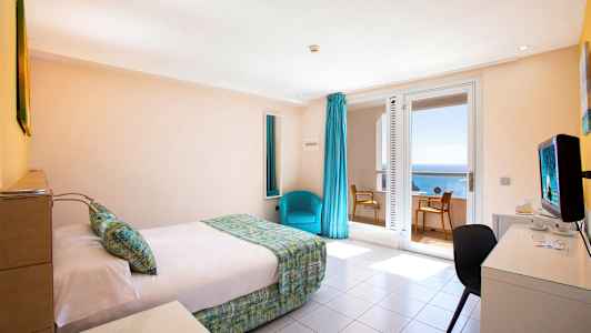 Ett hotellrum med en säng, ett skrivbord och en stol. Fönster med havsutsikt. (AI-genererad text)