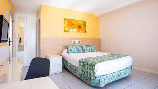 Ett hotellrum med en dubbelsäng, väggmålning av blommor ovanför sängen och ljusa väggar. (AI-genererad text)