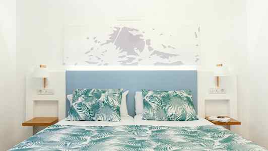 Säng med grön- och vitmönstrat täcke och kuddar, med blå sänggavel och vita väggar. (AI-genererad text)