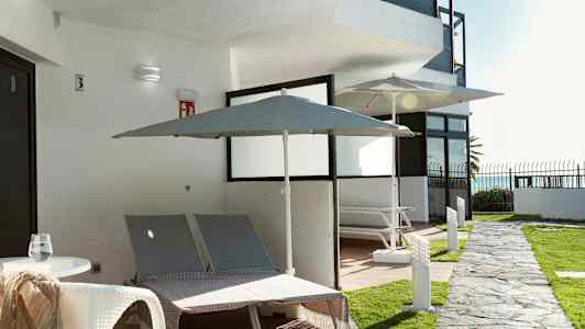 Utomhusvy med två solstolar och parasoller vid en byggnad. (AI-genererad text)