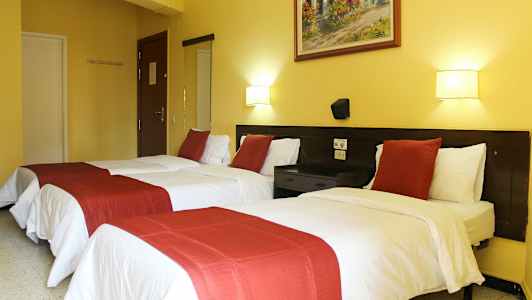 Hotellrum med två enkelsängar, vita lakan och röda dekorativa överkast. (AI-genererad text)