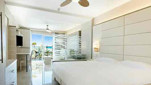 Ljust hotellrum med stor säng, glasparti och utgång till balkong. (AI-genererad text)