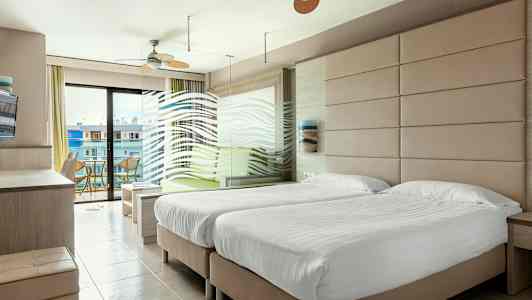 Ett hotellrum med två enkelsängar, en sittgrupp och en balkong med utsikt. (AI-genererad text)