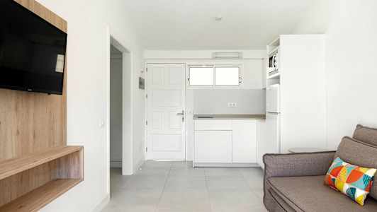 Ett vitt rum med en soffa, TV, trähylla och kök. (AI-genererad text)