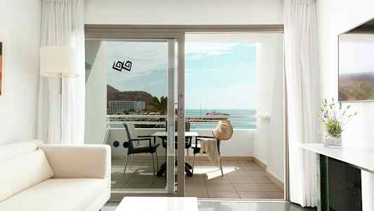 Modernt och ljust inrett vardagsrum med utsikt mot en balkong, som visar ett havslandskap. (AI-genererad text)