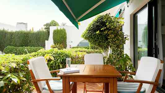 Utemöbler med tre stolar kring ett bord på en terrass, omgivna av grönska. (AI-genererad text)