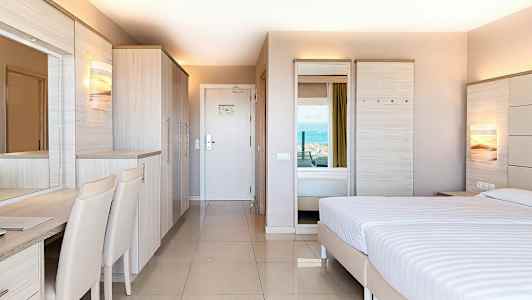 Ett hotellrum med modern inredning, en dubbelsäng, garderob och skrivbord, med utsikt mot havet. (AI-genererad text)