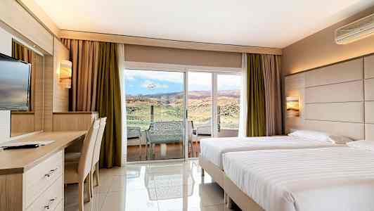 Hotellrum med två enkelsängar, skrivbord och utsikt mot landskap genom en glasdörr. (AI-genererad text)