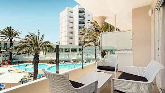 Vy från en terrass med plats för sittgrupp, utsikt över en pool och omgivande byggnader. (AI-genererad text)