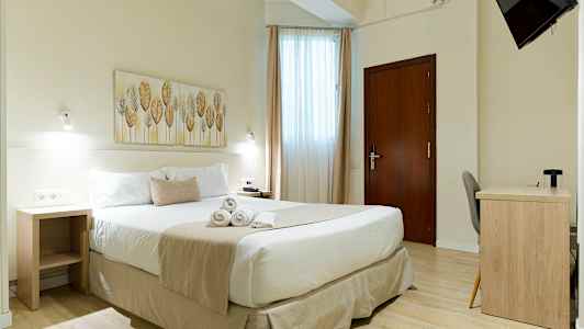 Ett ljust hotellrum med en dubbelsäng, ett skrivbord, och en väggmonterad TV. (AI-genererad text)