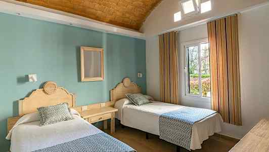 Två enkelsängar med trähuvudgavlar i ett hotellrum med en grön vägg och fönster. (AI-genererad text)