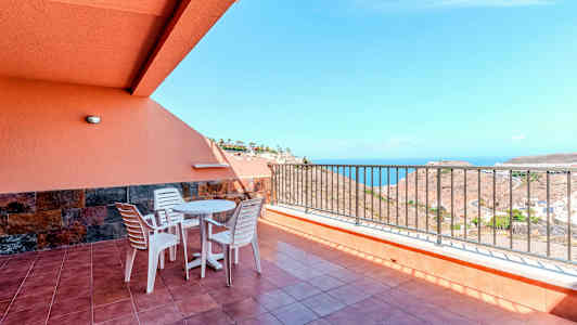 Terrass med bord, stolar och räcke, samt havsutsikt. (AI-genererad text)