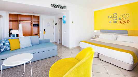 Hotellrum med modern inredning, inkluderande en säng, sittgrupp och färgglada detaljer. (AI-genererad text)