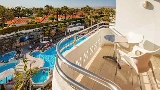 Utsikt från en balkong med bord och stolar mot en pool och palmer. (AI-genererad text)